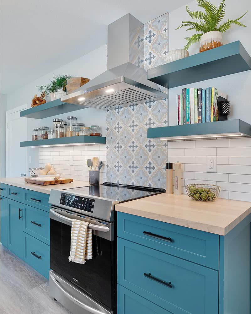 teal kitchen cabinets and floating shelves with patterned tile behind range hood
